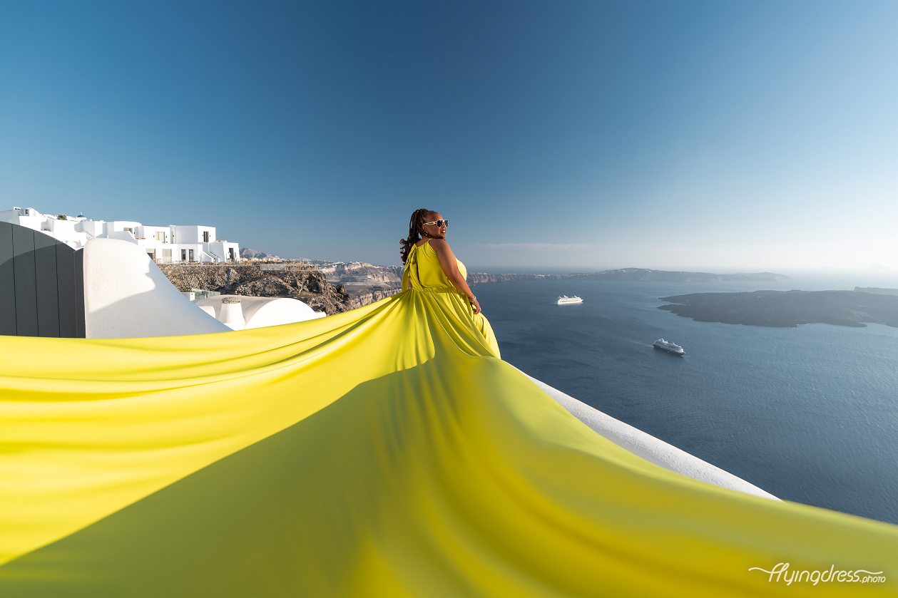 A wave of electric yellow silk billows over Santorini's whitewashed rooftops against the endless blue of the Aegean.